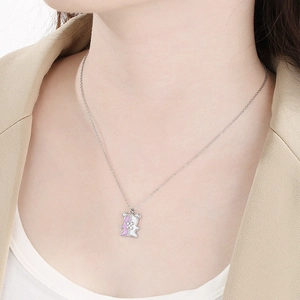 Close-up of a silver bear pendant necklace with pink and white enamel on a model