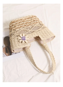 Close-up of beige woven straw tote bag with floral applique and intricate hollow patterns