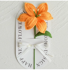 Detail of a handmade orange crochet lily flower on a white card with an elegant ribbon