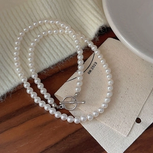 Detailed close-up of a pearl necklace with a silver OT clasp on a cozy knit background