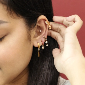 Gros plan de plusieurs boucles d'oreilles créoles dorées avec zircons sur l'oreille