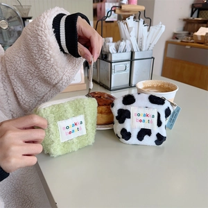 Detailed close-up of plush mini makeup bags in sage green and cow print on cafe table