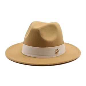 Detail of wool fedora hat with beige decorative band and golden metal M emblem