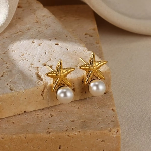 Detail of gold starfish earrings with round pearls on a natural stone surface