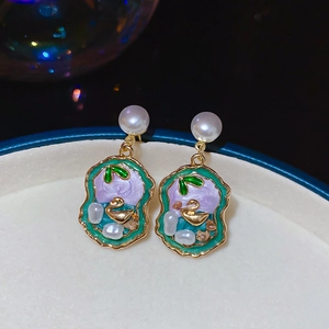 Macro shot of gold swan earrings with green enamel and pearl inlay on a tray
