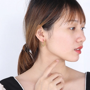 Gros plan d'une boucle d'oreille créole en forme de U à perles dorées sur un mannequin