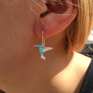 Close-up of hummingbird drop earring with blue gradient enamel worn on a model's ear