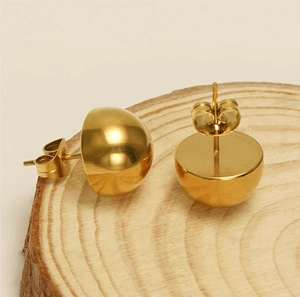 Macro shot of polished gold dome stud earrings on a natural wood ring pedestal