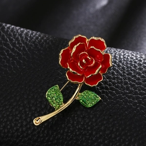 Elegant red rose brooch with green crystals and gold finish on black leather background