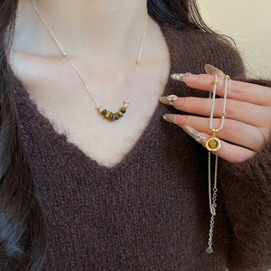 Macro view of tiger eye stone pendant and beaded silver necklace on brown sweater