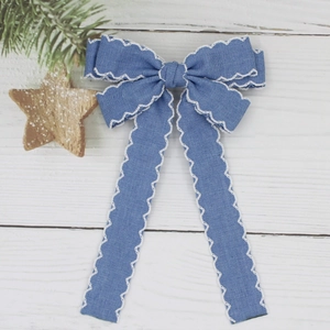 Close-up of blue denim bow hair clip with white scallop embroidery on a wooden surface