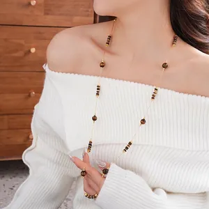Long collier élégant en perles d'œil de tigre avec détails dorés sur un pull blanc
