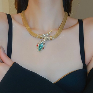 Macro detail of a gold snake necklace featuring sparkling green and red crystal eyes
