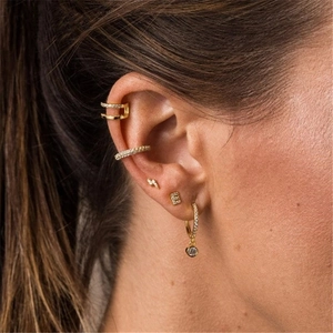Close-up of gold ear cuff set with rhinestones and geometric stud earrings worn by a model