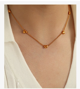 Close-up of a delicate gold heart pendant necklace worn on a white knit collar