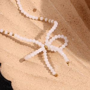 Détail d'un collier en perles de cristal blanc avec un nœud papillon doré élégant
