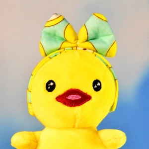 Detailed close-up of a cute yellow plush duck pendant featuring a green bow headband