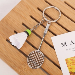 Detailed close-up of a silver badminton racket and shuttlecock keychain on a wooden tray
