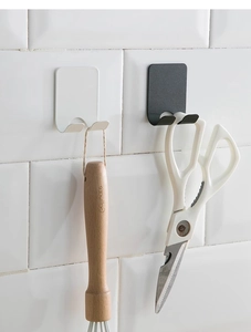 Detail of self-adhesive wall hooks in black and white holding kitchen tools on tiles