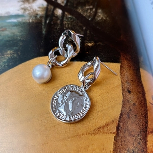 Detail of asymmetric pearl earrings with vintage coin pendant and silver chain links