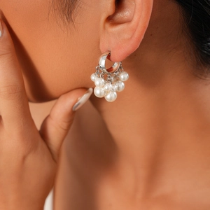 Close-up of silver C-shaped hoop earrings with dangling white pearl clusters on model
