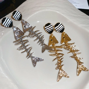 Detailed shot of gold and silver fish bone earrings with black and white enamel discs
