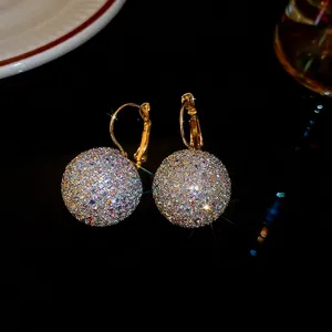 Elegant gold earrings with shimmering crystal pavé ball pendants on a dark reflective surface