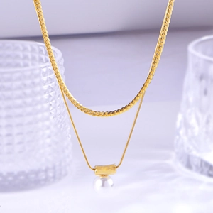 Double-layer gold necklace with flat snake chain and pearl pendant on a glass background