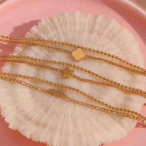 Detail of gold clover star and feather charms on beaded and figaro chains over coral
