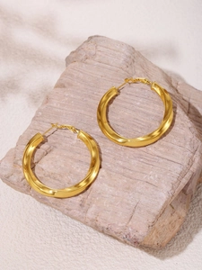 Macro shot of twisted gold-plated hoop earrings on textured stone showcasing metallic details
