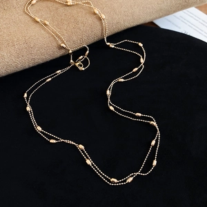 Detail view of a layered gold-plated beaded necklace with tiny rice-shaped metal beads