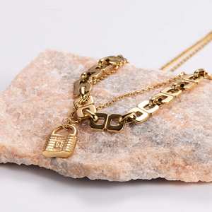Golden padlock pendant necklace with mixed thick and thin chains on natural stone