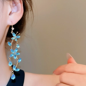 Detailed close-up of a blue floral tassel earring featuring sparkling cubic zirconia on a model