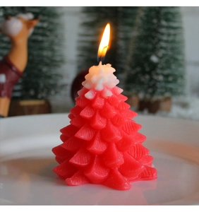 Close-up of a burning red Christmas tree candle with white snow detail and warm light