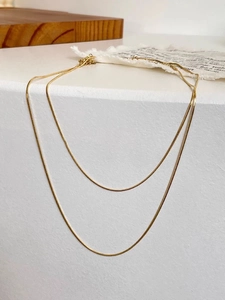 Detalle de collares de cadena de serpiente dorados minimalistas sobre fondo geométrico moderno