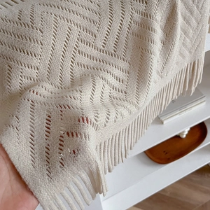 Detail of beige hollow knit shawl showing delicate fringe and wavy textured pattern