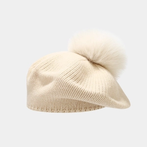 Detail of beige knitted beret showing soft wool texture and large fluffy faux fur pompom