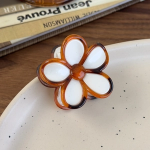 Detail view of the amber floral hair claw clip on a ceramic tray with a wooden background