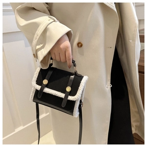 Close-up of black leather crossbody bag with white faux fur trim and gold metal buckles