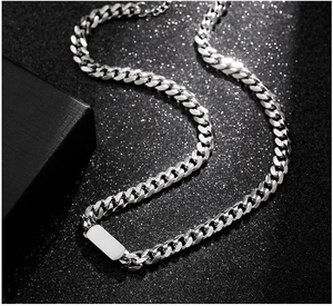 Close-up of a silver Cuban link necklace with a blank rectangular metal pendant detail