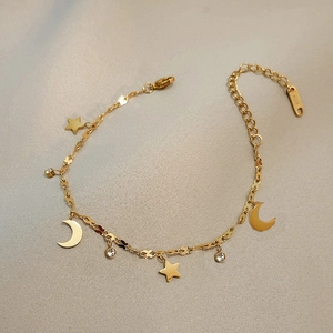 Elegant 18K gold star and moon anklet with crystals on a textured gray background