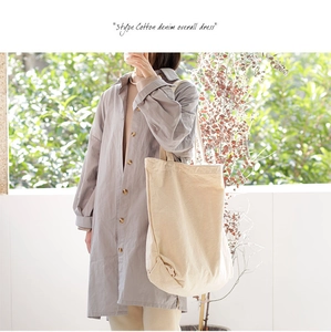 Lifestyle shot of a beige canvas tote bag worn with a grey dress in sunny outdoor lighting