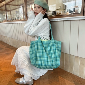 Detail of green plaid canvas tote bag with yellow lining worn by model in a cafe