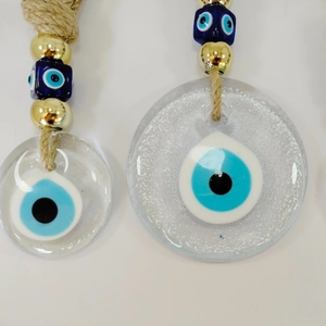 Detail of glass Evil Eye pendants with golden beads and twine on white background