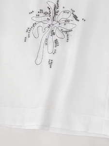 Detailed view of intricate beadwork and floral embroidery on a white fabric surface