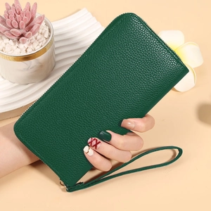 Detail of dark green long wallet with lychee texture and wrist strap held by hand