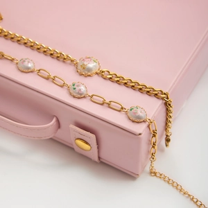 Close-up of retro gold link bracelet featuring white enamel beads with pink floral patterns