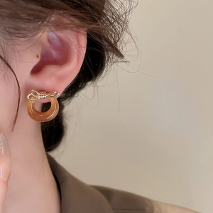 Macro shot of vintage style earrings with golden bow and amber resin ring on a model