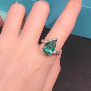 Pear-cut green tourmaline ring with criss-cross pavé diamond band on female hand