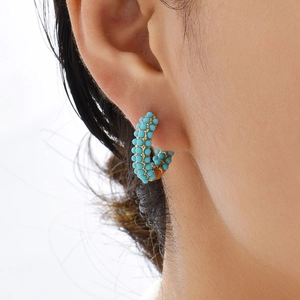 Close-up of bohemian C-shaped 18K gold earrings with turquoise and pearls on a model